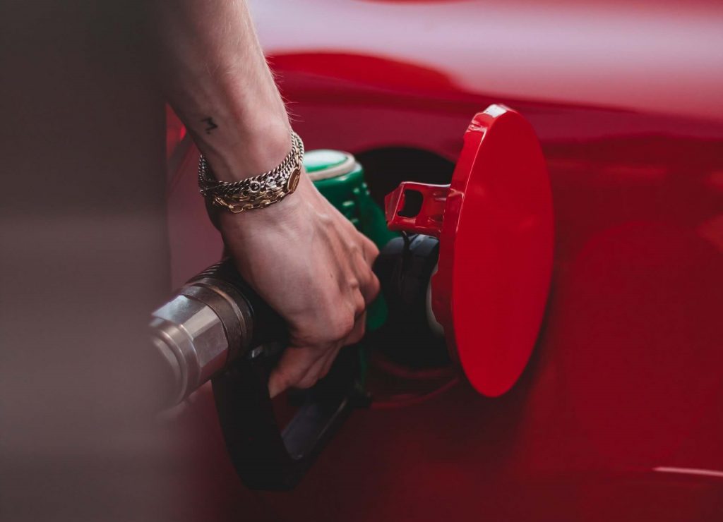 Una persona de pie en una gasolinera, llenando un coche de combustible, haciendo hincapié en la practicidad de repostar